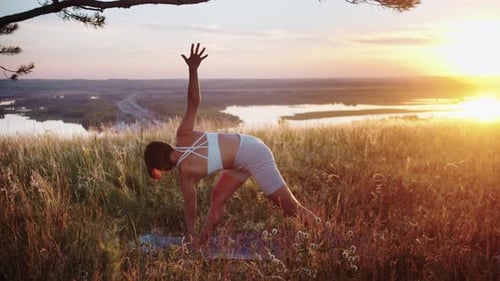 Femme asiatique sportive dans un haut de sport faisant du yoga sur la colline au coucher du soleil