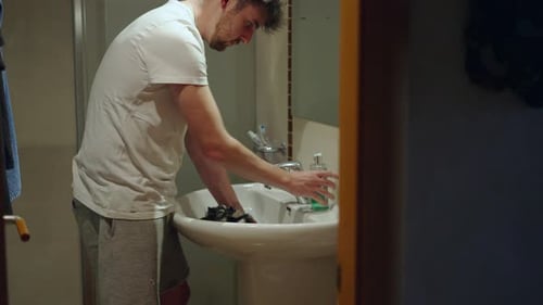 Young Caucasian Man Using Shampoo to Clean His Guinea Pig Pet Inside the Sink