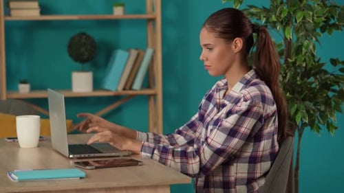Medium Shot Capturing a Woman Working on a Laptop in Her Home Office and Drinking Coffee Young