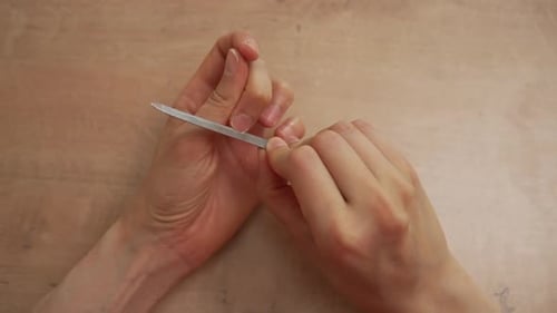 Geheimnisvolle Person, die Fingernägel mit einer Metallnagelfeile auf einem rustikalen Holztisch feilen und formen