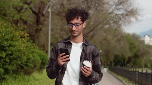Young Man Using Smartphone While Walking in a Park