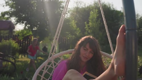 Woman reading in a swing with child nearby