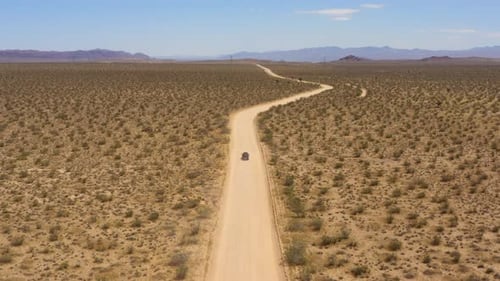 Black SUV approaches a curve in an otherwise straight road through the plains in the Mojave Desert o