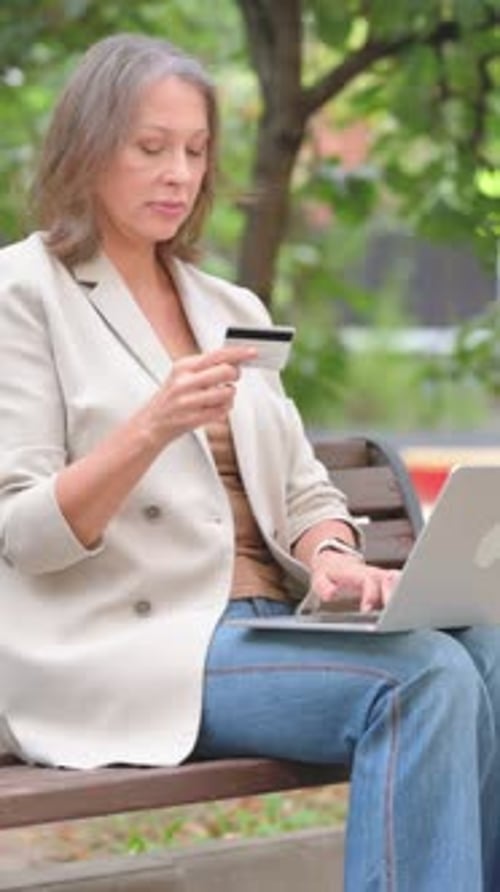 Woman uses laptop and credit card in park