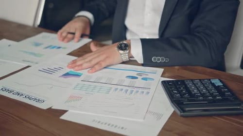 Close Up of a Businessman Hands with Pen Working at Office Desk and Analyzing Graphs and Charts and