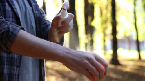 Man spraying tick repellent onto arm in park, closeup