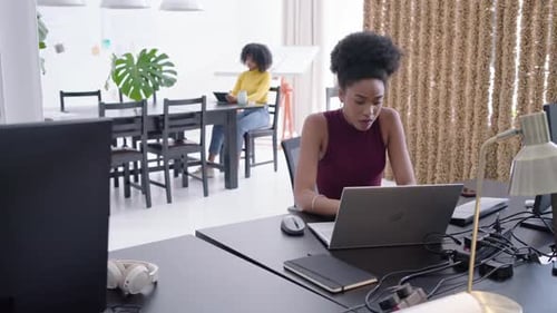 Une équipe féminine diversifiée en studio, une femme à l'avant tape sur un ordinateur portable, jetant un coup d'œil sur une tablette pointant vers le travail