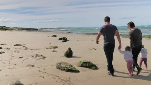 Parents with twins walking hand-in-hand down beautiful secluded beach, sunny day