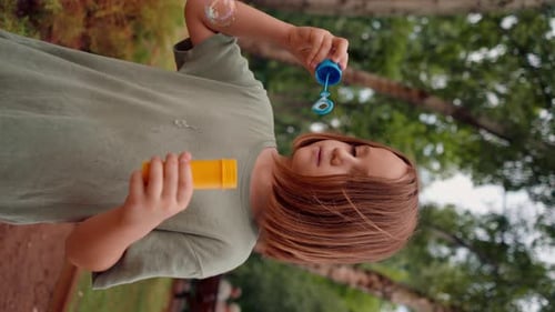 vertical video portrait beautiful cute little girl blowing soap bubbles in city park happy carefree