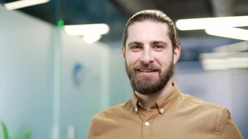Portrait of smiling bearded businessman standing at workplace in modern business office.