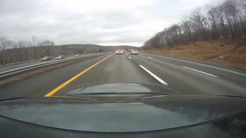A black car is driving on the road and video of the road is being shot from the rood of the car. The