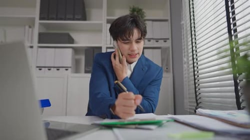 Asian busy businessman talking phone and using laptop working in office.