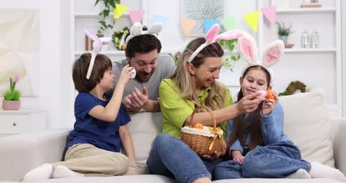 Easter celebration. Happy family with bunny ears and painted eggs on sofa at home