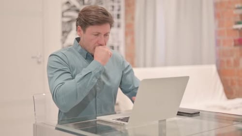 Man Working At Desk Coughs into Hand