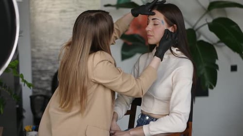 Aesthetician Shaping Young Woman's Eyebrows in Bright Studio