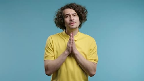 Young Adult Clasping Hands in Front of Light Blue Background