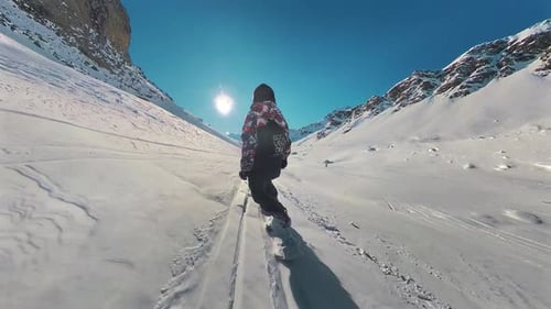 Back view of snowboard freeride. Professional snowboarder ride down the mountain slope at sunny wint