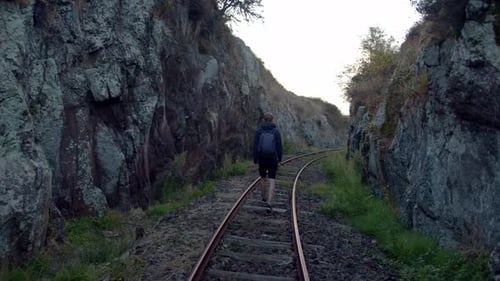 Einsamer junger Mann, der auf Bahngleisen zwischen Felsformationen läuft. Dunkel