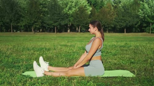 Beautiful sports girl in is engaged in stretching on a sports mat in a city park. Yoga in a sunny me