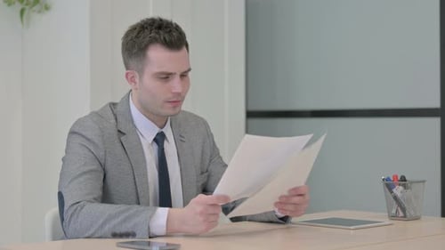 Young Businessman Reading Documents in Office, Paperwork
