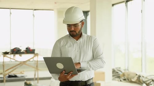 Indian Construction Engineer Using Laptop for Project Analysis on Site