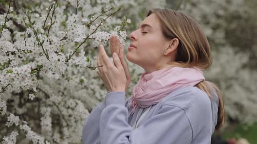 Side View of Beautiful Female Allergic to Spring Flowers Sneezing While Smelling White Flowers