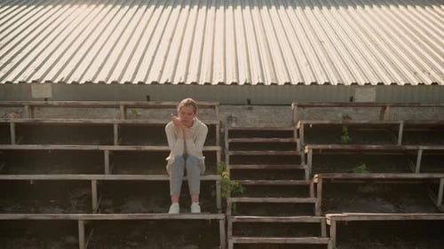 Pensive Woman Reflecting on Rustic Stadium Bleachers in Warm Sunlight
