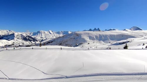 Toma aérea en movimiento sobre un telesilla y una pista de esquí en una zona de deportes de invierno cubierta de nieve, con una montaña lejana