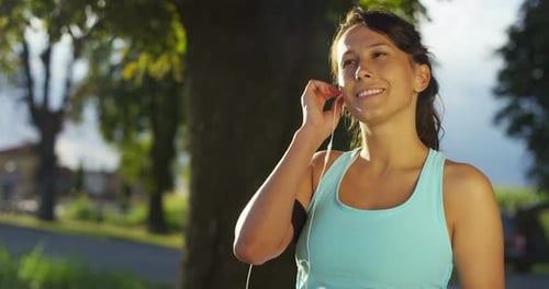 Smiling Woman Putting in Earphones in a Park