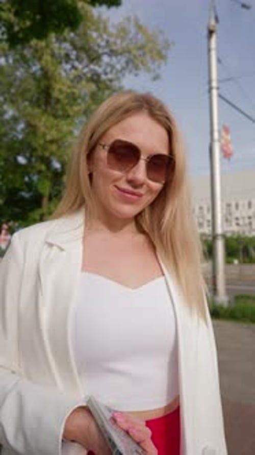 Smiling Woman in Sunglasses Stands on Urban Sidewalk