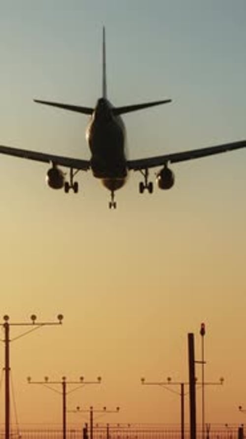 An Airplane is Shown Landing at Sunset in a Vertical Video While Approaching the Runway