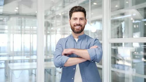 Porträt eines lächelnden erfolgreichen Geschäftsmannes, der mit verschränkten Armen am Arbeitsplatz in einem Unternehmen steht