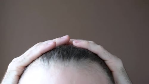 Man touching her hair close-up on brown background, hair loss concept.