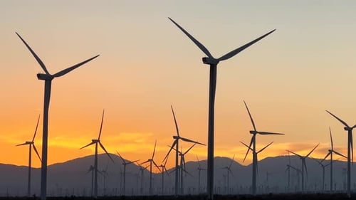 A field of wind turbines during a colorful sunset with mountains in silhouette in the background
