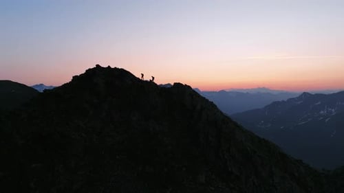 Two mountaineers walking on a ridge in the Alps before sunrise. Drone footage.