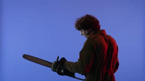 Man in White Mask with Chainsaw in Hands on Blue Background with Red Neon Light Image of Jason
