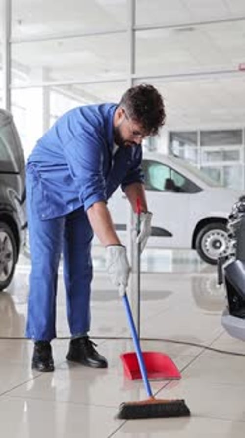 Un concierge balayant le sol carrelé chez un concessionnaire automobile