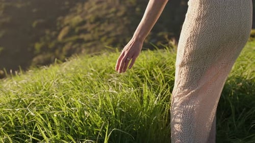 Woman Walking Through Lush Green Field Wearing a White Dress at Golden Hour Feeling Nature Freedom
