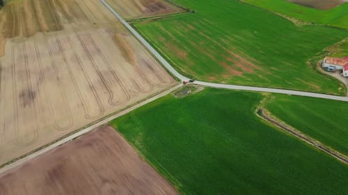 Aerial shot of a farmer driving his tractor in rural countryside roads in Norway