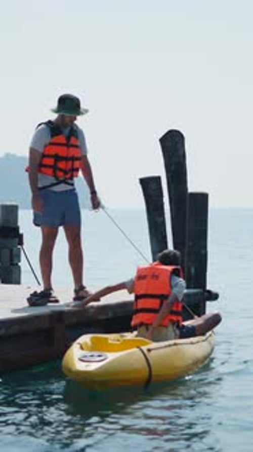Two Young Men Untie a Kayak From the Dock and Climb on It to Paddle