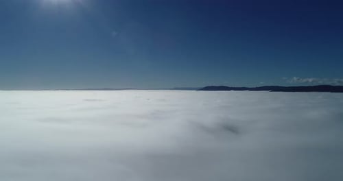 Aerial footage flying above clouds with blue rolling hills in the background.