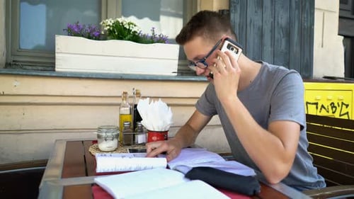 Young boy with cellphone and notebook studying at a cafe table