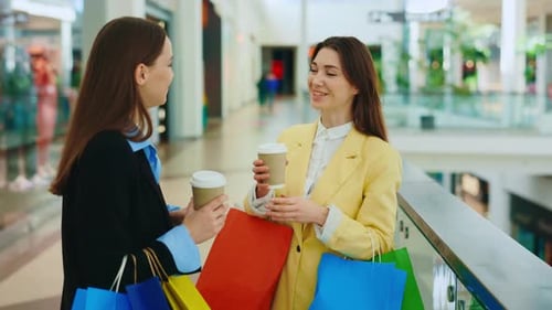 Two Happy Female Friends Standing in the Shopping Mall Womans Holding Coffee Laughing Speaking with