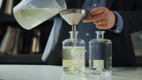 Male expert pouring distilled gin in a glass bottle with a funnel, quality control process in a gin