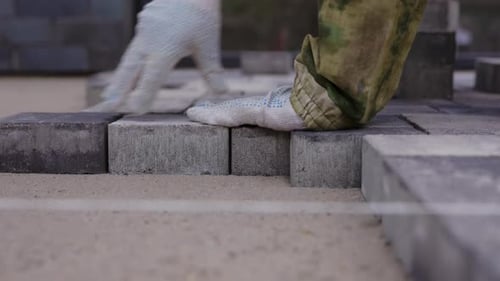 Worker Laying Concrete Paving Blocks During Pavement Installation