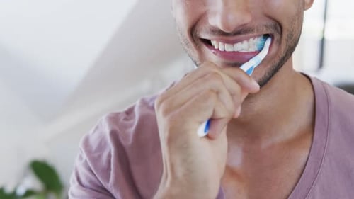 Close up of happy biracial man brushing teeth in sunny bathroom in the morning, slow motion