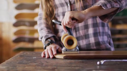 Video of midsection of caucasian female skateboarder fixing skateboard in skate shop