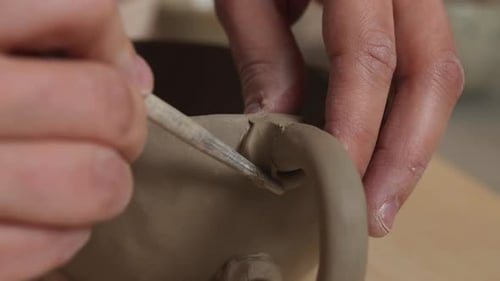 Close up shot of white hands making mug and molding clay with a brush