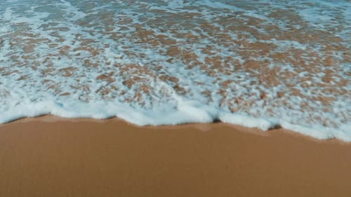 Slow-motion shot of a wave crashing to the beach. Beautiful evening colour of the sand.