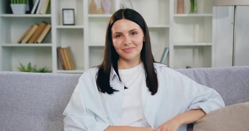 Close-up. Portrait smiling beautiful woman looking at camera sitting on sofa alone at home.